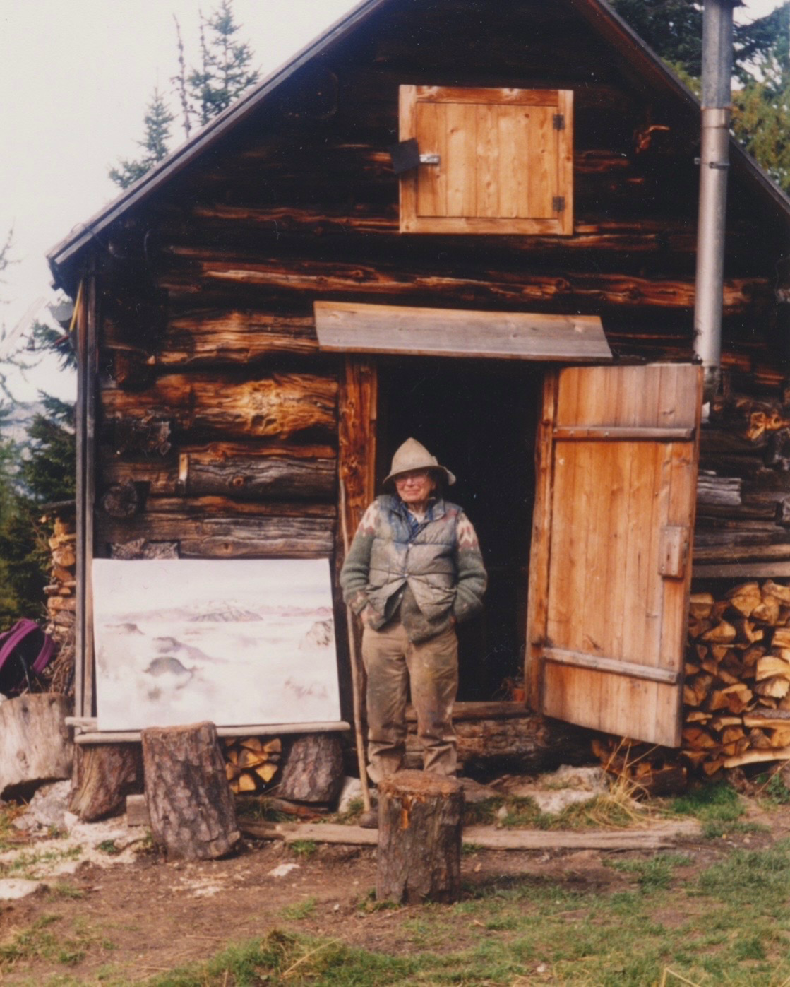 Edith Kramer outside a wooden mountain cabin with a painting